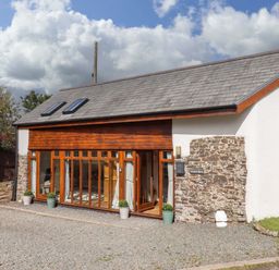 An exterior view of a building with large windows and stone wall at Church Barn Sutcombe near Bradworthy
