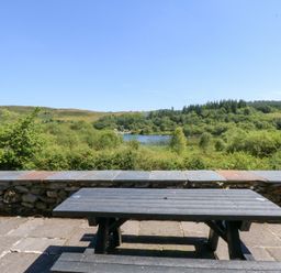 A picnic table with a view of a lake and surrounding hills at Ty Newydd