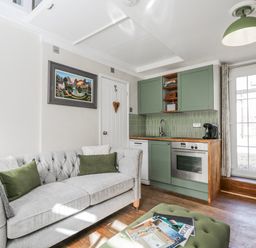 A living room with a sofa and kitchen area at Firefly Cottage