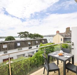 A balcony with a table and chairs overlooking water at 9 Slipway Cottages in Rock