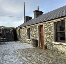 An outdoor view of a stone house with a table and barrel at Cobble Stone Cottage near Leabgarrow, County Donegal
