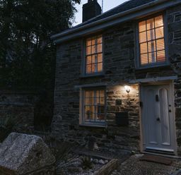 A stone house with lit windows and a door at Tamarisk Cottage in St. Agnes