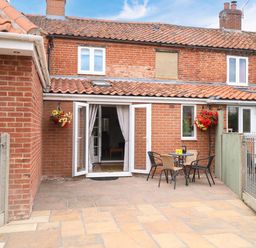 An outdoor patio with seating and a table at Honeysuckle Cottage in Swaffham