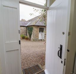 An entrance with an open door leading to a gravel garden at Honeymug in Branton near Powburn