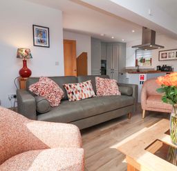 A living room with a sofa, armchairs, and a kitchen area at Butterfly Days in Bideford