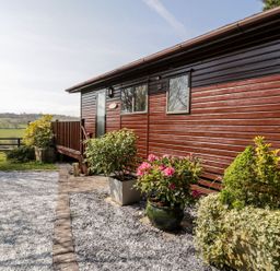 A wooden building with deck and flower pots at Summertime Lodge in Rhyd-y-Foel near Abergele