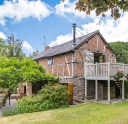 A brick and timber house with a wooden balcony and garden at The Cider Mill in Westhope near Leominster