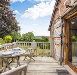 An outdoor wooden balcony with a round table set for two and wooden chairs overlooking a garden at The Cider Mill in Westhope near Leominster