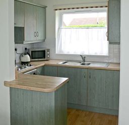 A kitchen with wooden countertops cabinets a microwave kettle double sink and a window at Seascape in Kessingland near Lowestoft