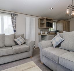 A living room with sofas and a kitchen area at Grasmoor View Lodge