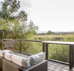 An outdoor patio with a sofa and table overlooking a field at The Larch House in Farndon