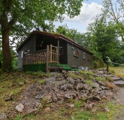 A cabin with a deck surrounded by trees at Oak Lodge near Mynydd Cerrig