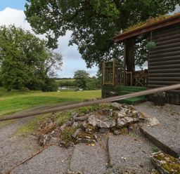 An outdoor view of a cabin with a deck and gravel path at Oak Lodge in Mynydd Cerrig near Porthyrhyd