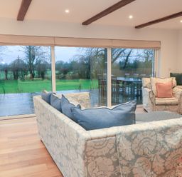 A living room with a sofa and armchair overlooking a garden at Peewit Coach House in Moreton-in-Marsh