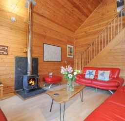 A living room with red sofas, a table, and a stove at Pencarrow in St Breward