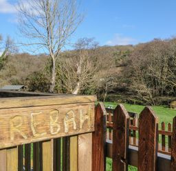 A wooden sign labeled Trebah with a fence and trees in the background at Trebah in St Breward
