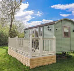 A green cabin on a wooden deck surrounded by trees at The Dragonfly in Bewholme near Hornsea