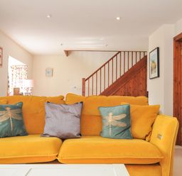 A living room with a yellow sofa and decorative pillows at Rosewin Farmhouse near St Minver