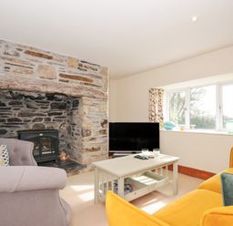 A living room with a fireplace and a television at Rosewin Farmhouse near St Minver