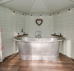 A bathroom with a silver bathtub and wine bottle on a shelf at Y Cwlwm in Lampeter
