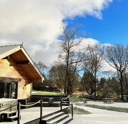 A wooden cabin with a deck and hot tub in a snowy outdoor area at Dwrgi Aber near Llanybydder