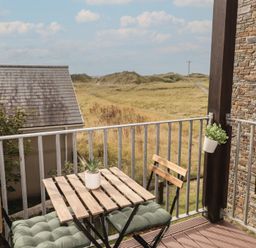 A balcony with a table and chairs overlooking a grassy area at Awel y Môr in Burry Port