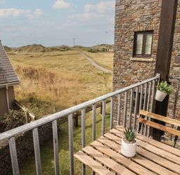 A balcony with a table and chairs overlooking a grassy area at Awel y Môr in Burry Port