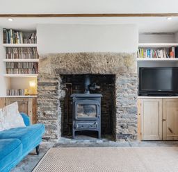 A living room with a wood stove and shelves at Treovis Cottage in Callington
