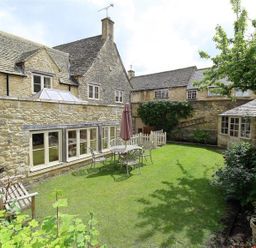 A garden with a stone house and seating area at The Coach House in Burford