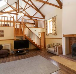 A living room with a television, stairs, and a fireplace at Millbarn in Crowcombe