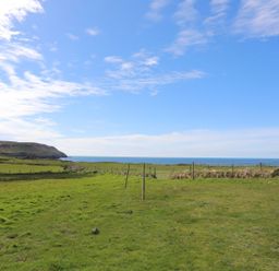 A grassy area with a fence and ocean view at Fadrun - 3 Ty'n Don
