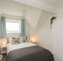 A bedroom with a bed, curtains, and a wardrobe at Penrhyn - 4 Ty'n Don