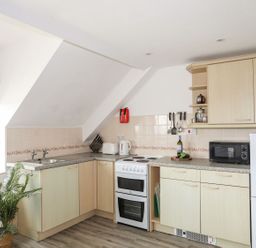 A kitchen with cabinets, stove, microwave and sink at Towyn - 7 Ty'n Don