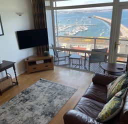 A living room with a television and furniture overlooking the harbor at Snowy Owl View at The Breakwater in Brixham
