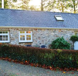 A stone cottage with windows and a door surrounded by a hedge at Corner Cottage in Maenclochog