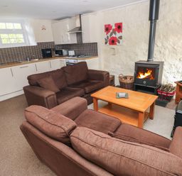 A living room with a wood stove and kitchenette at Stable Cottage in Clarbeston Road