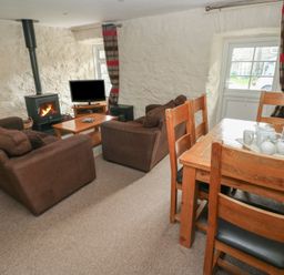 A living room with a sofa, dining table and wood stove at Stable Cottage in Clarbeston Road