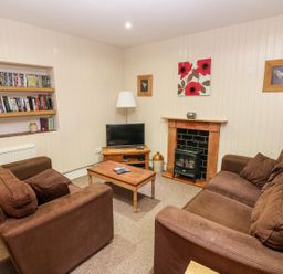 A living room with a television, sofa, and bookshelf at Lake Cottage in Clarbeston Road