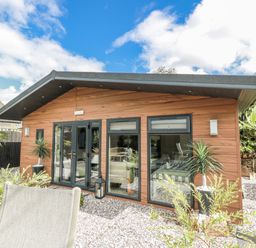 A cabin exterior with windows and plants in the garden at Cabin At The Brig Annan