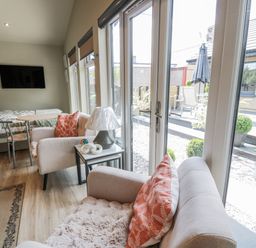 A conservatory with a sofa, armchair, table, and television at Cabin At The Brig in Annan