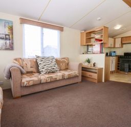 A living room with a sofa and kitchen area at Hideaway Lodge in Abergele