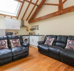 A living room with a sofa and kitchen area at The Owl Barn Cottage