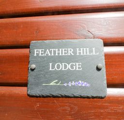 A sign displaying Feather Hill Lodge attached to wood at Feather Hill Lodge White Cross Bay near Troutbeck Bridge