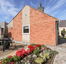 An outdoor area with a table and chairs next to a flower bed at Gelli - Morfa Nefyn