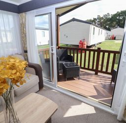 A living room with a view of a deck and flowers in a vase at Stag Lodge, Caravan 70 Great Yarmouth