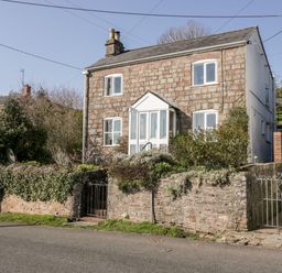 A stone house with white framed windows and a front porch behind a low stone wall with greenery at Gordons View Pleasant Stile near Gloucester