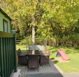 a garden area with a table and chairs near a tree and a small slide at Hafan y Mor Haven - Holiday Accommodation 11370 in Pwllheli
