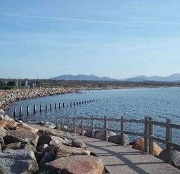 a coastal scene with a pathway along the shore and mountains in the distance at Hafan y Mor Haven - Holiday Accommodation 11370 Pwllheli