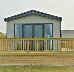 a wooden deck in front of a holiday home with large windows at Perran Sands - Holiday Accommodation 12174, Perranporth