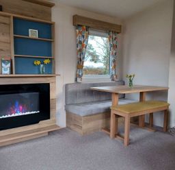 a dining area with a table and bench seating near a modern fireplace at Hafan y Mor Haven - Holiday Accommodation 12637 in Pwllheli